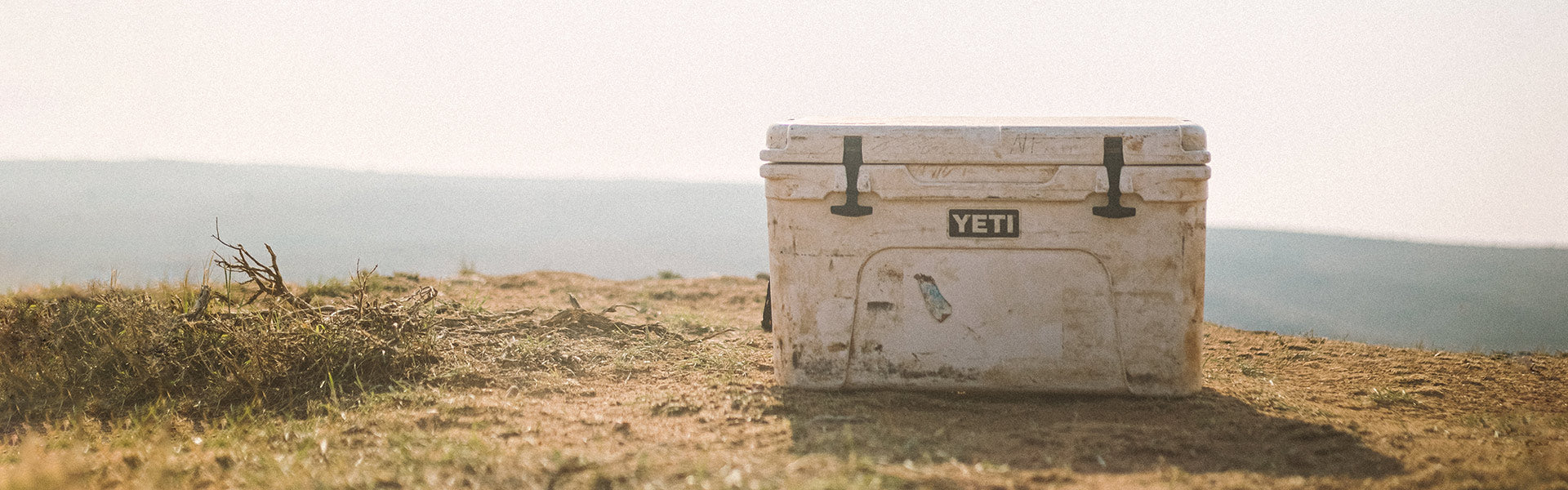 Well used yeti cooler box on a grassy hillside with a scenic background
