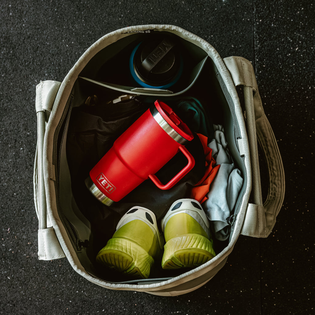 Open bag with Rescue Red Rambler® Travel Straw Mug, green shoes, and other items on a dark surface