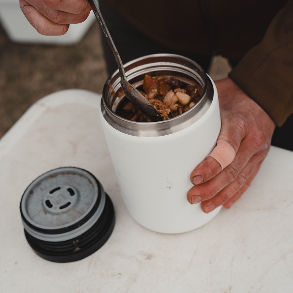 Person holding a white YETI food jar with food, sitting on a white surface.