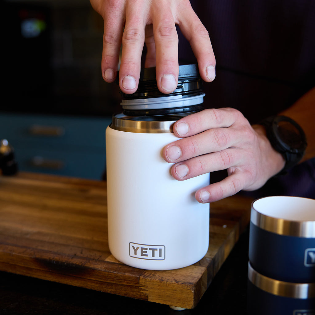 Person holding a YETI food jar on a wooden surface.