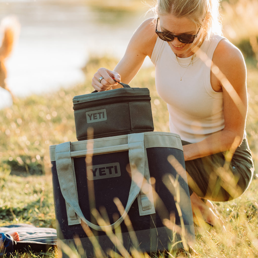 Woman opening a YETI cooler outdoors in a natural setting