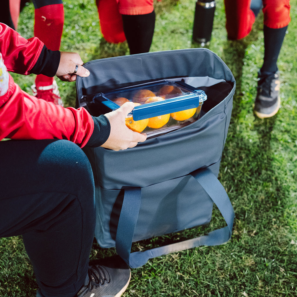 Person opening a YETI cooler bag filled with oranges on grass