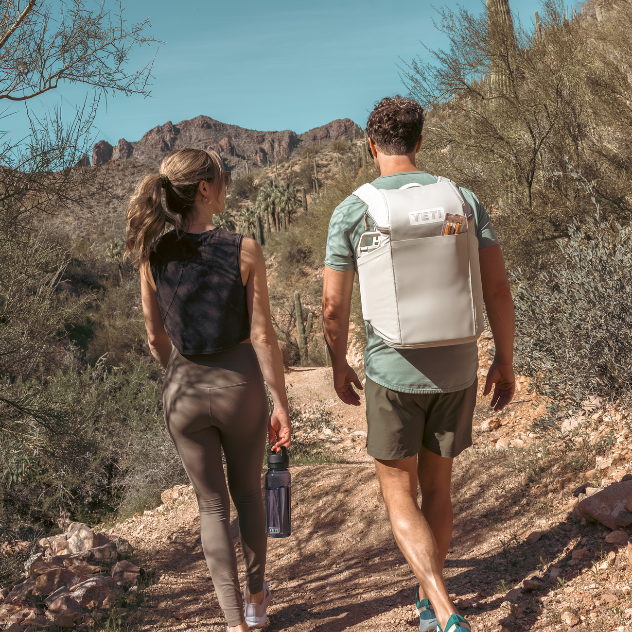 Two people hiking in a desert landscape with mountains in the background.