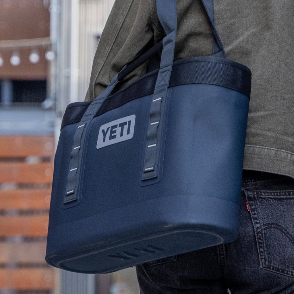 Person carrying a navy YETI cooler bag outdoors.
