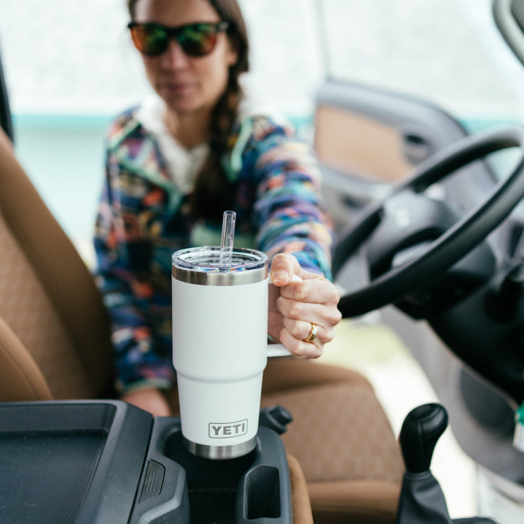 Person sitting in a vehicle holding a white YETI mug with a straw.