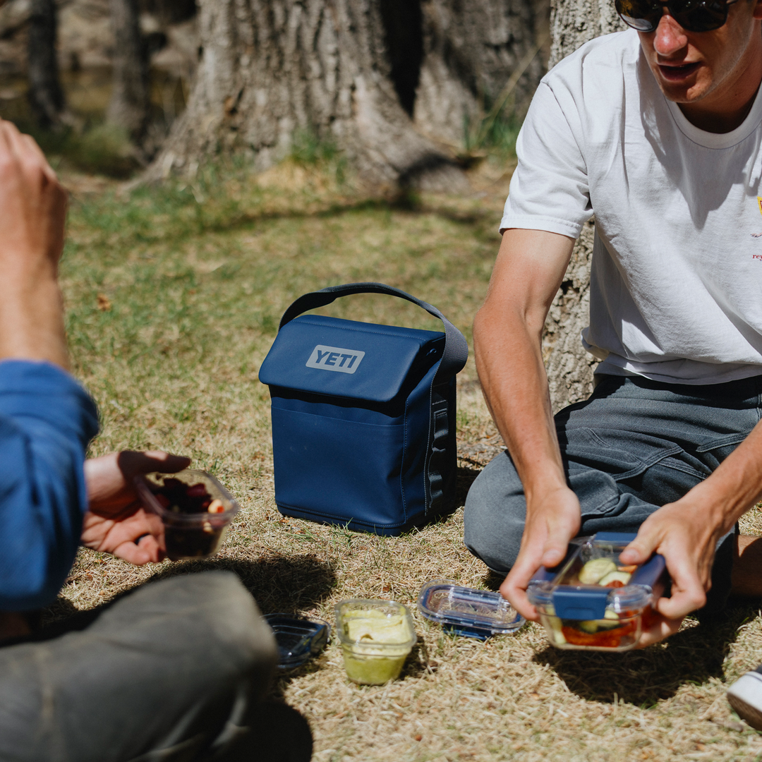 Two people having a picnic with a YETI cooler bag in a natural setting.