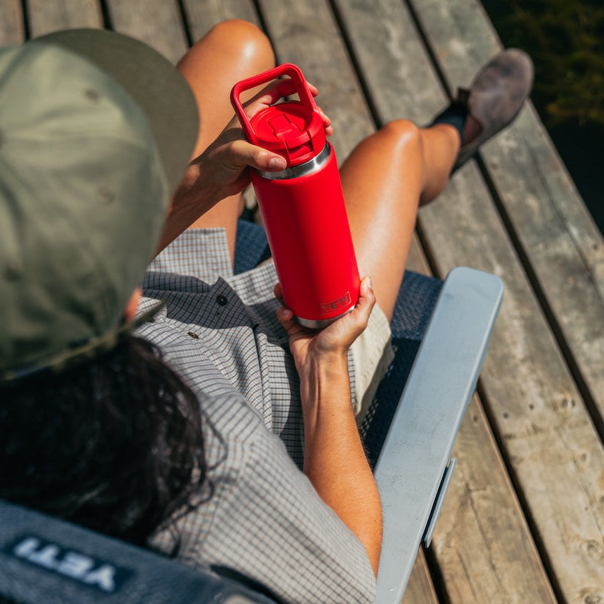 Person sitting on a wooden dock holding a red YETI water bottle.
